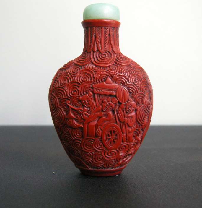 Cinnabar lacque snuff bottle on metal decorated and sculpted with a rider on one side and characters on a trolley on the other